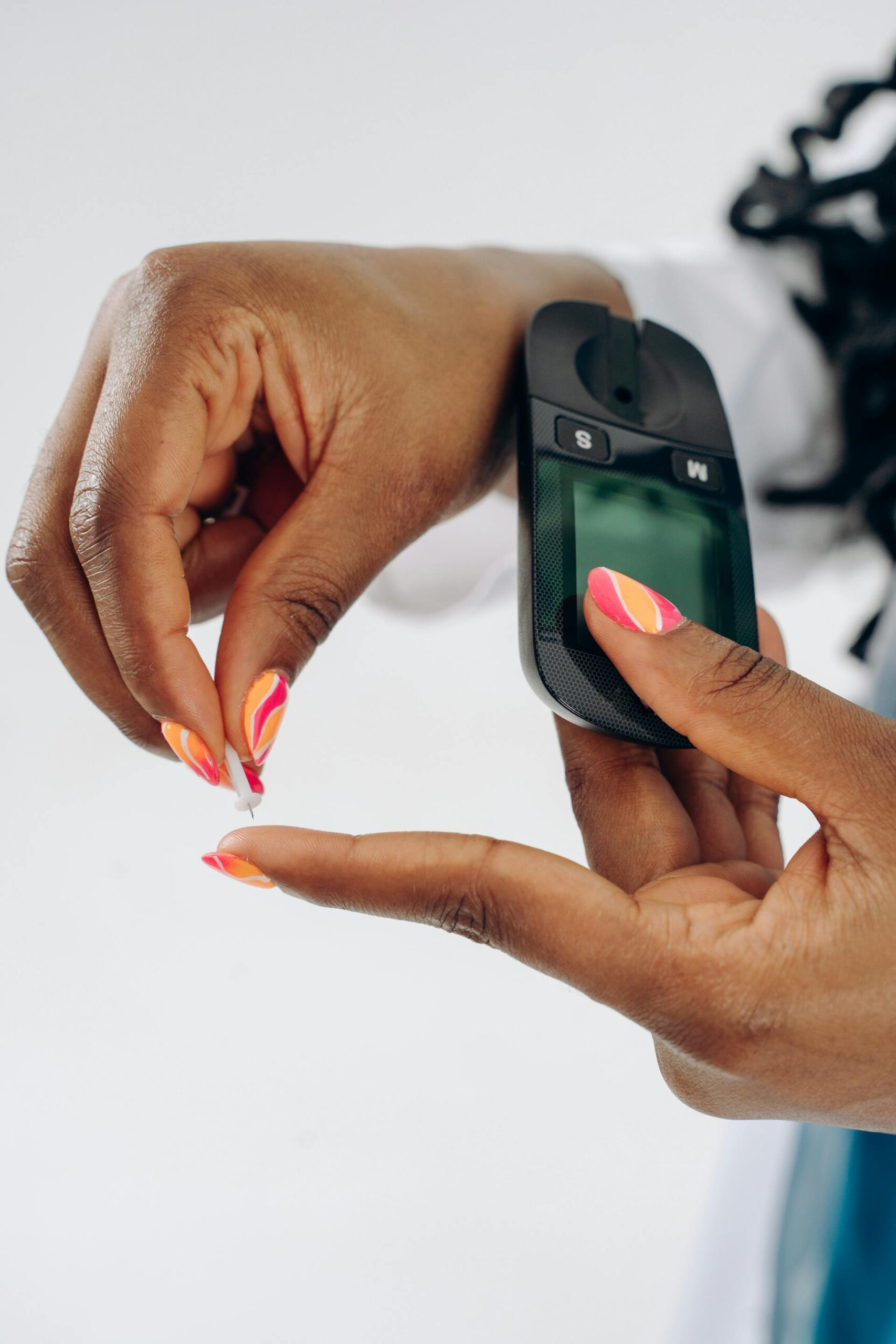 A person with vibrant, patterned nails using a blood glucose meter to check their blood sugar levels, preparing to prick their finger with a lancet. A person with vibrant, patterned nails using a blood glucose meter to check their blood sugar levels, preparing to prick their finger with a lancet.